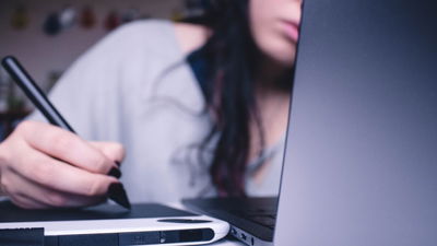 A photograph of a woman drawing on a computer tablet.