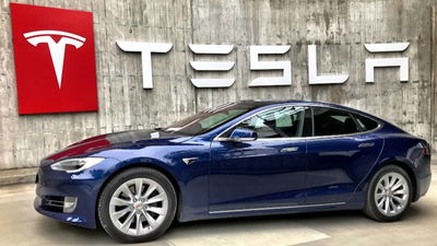 Tesla in front of Tesla sign.